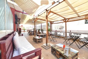 Un espacio al aire libre con mobiliario de madera, una mesa de vidrio y un banco de madera.
