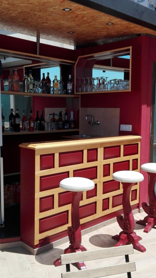 Zona de bar con diseño rojo y de madera, que incluye una barra con botellas y vasos, y tres taburetes.