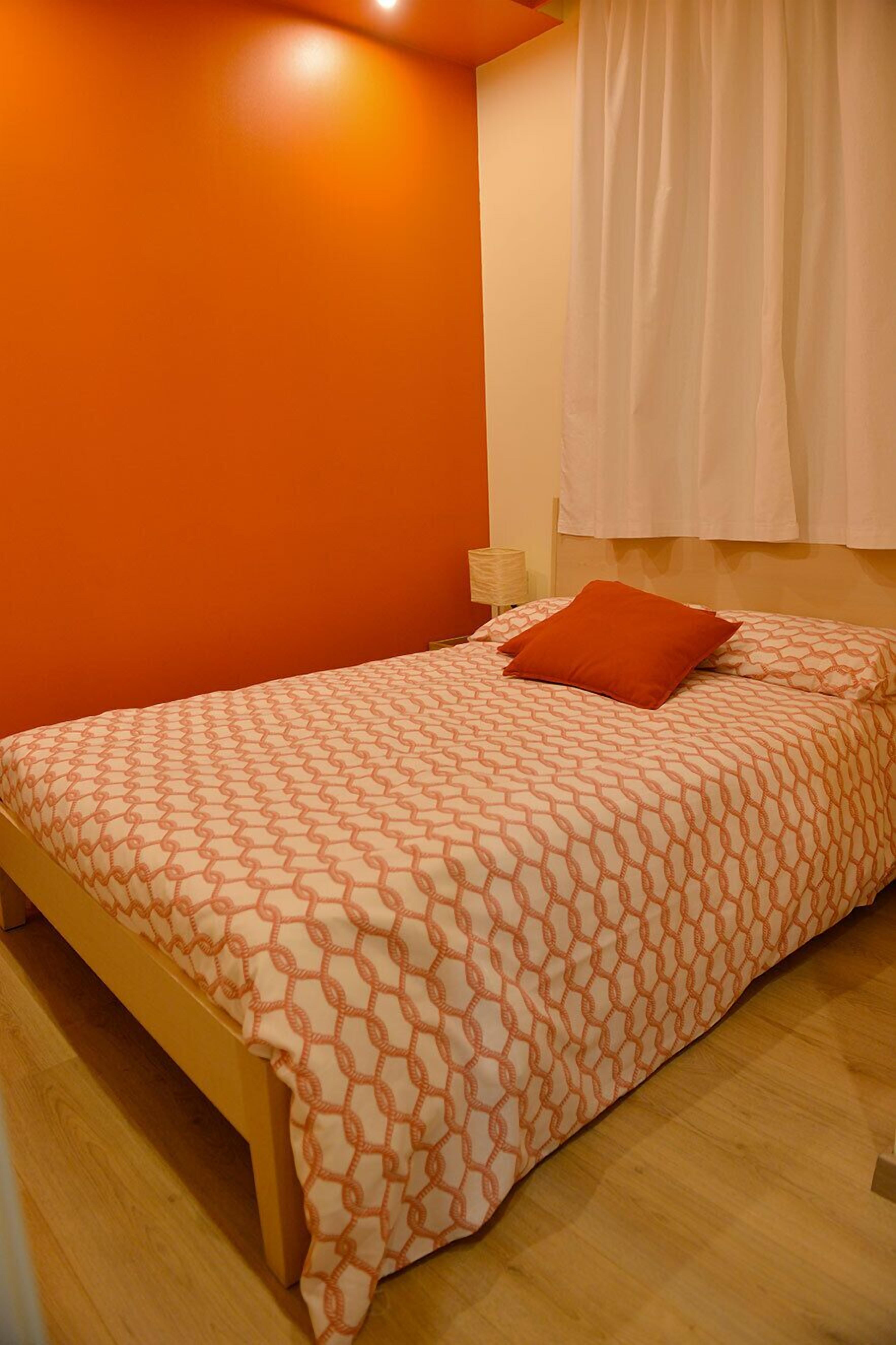 A bedroom with a bed, orange walls, and a window with curtains.
