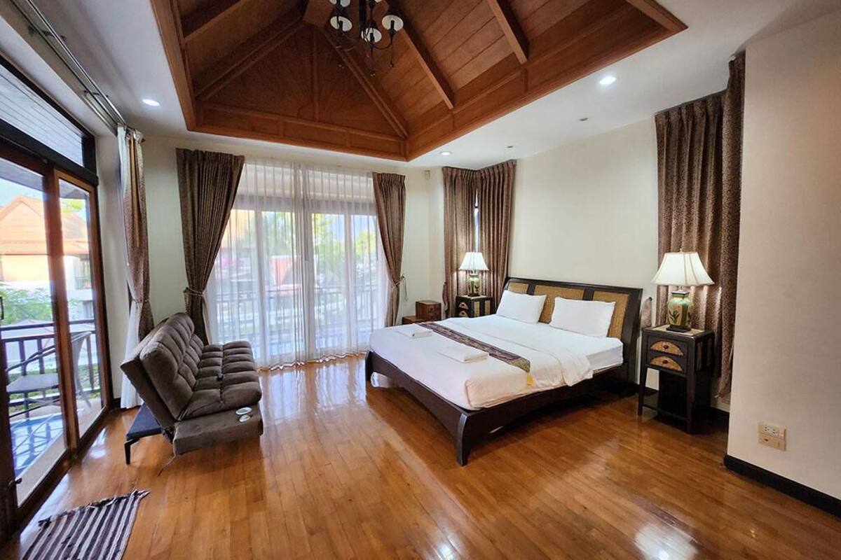 A spacious bedroom with a large bed, wooden ceiling, and a balcony view.