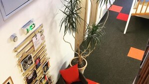 A reception area with a reception desk, a potted plant, a seating area with a sofa and a chair, and a wall with framed pictures and a fire extinguisher. - Tourhotel (Béthune)