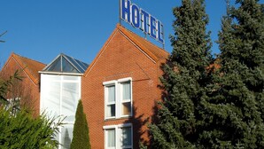 A hotel with a prominent sign, a brick facade, and a well-maintained garden with various plants and a tall coniferous tree. - Tourhotel (Béthune)