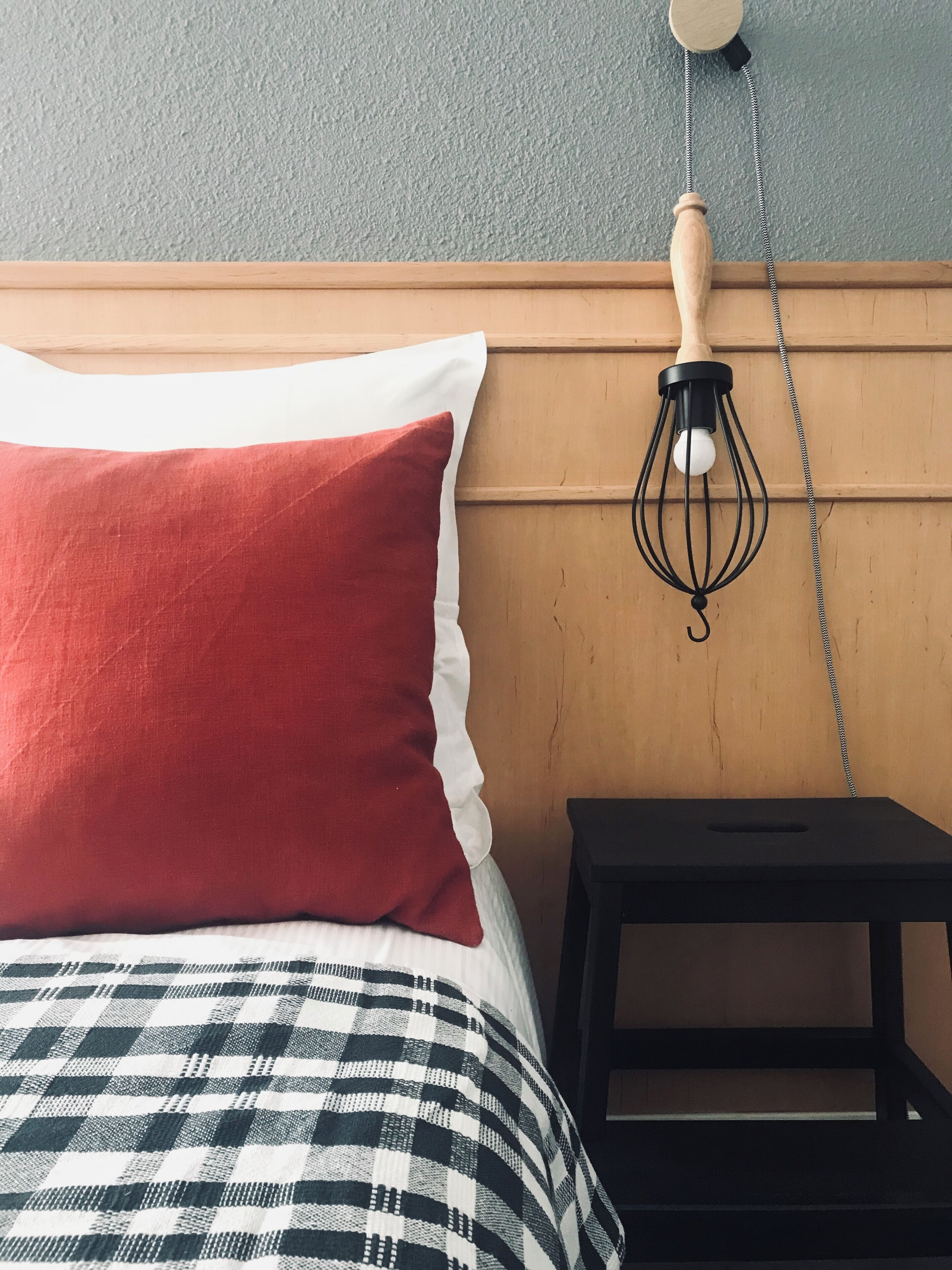 Un letto con una coperta a quadri, un cuscino rosso e una testiera in legno.