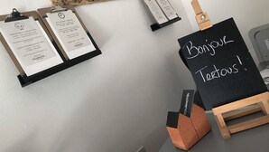 A room with a chalkboard displaying 'Bonjour Tertous!' and several items on a wall, including a map and a framed certificate. - Tourhotel (Béthune)