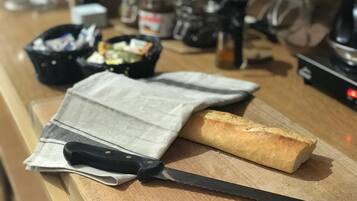 Una encimera de cocina con hogaza de pan, un cuchillo, un paño y diversos utensilios de cocina.