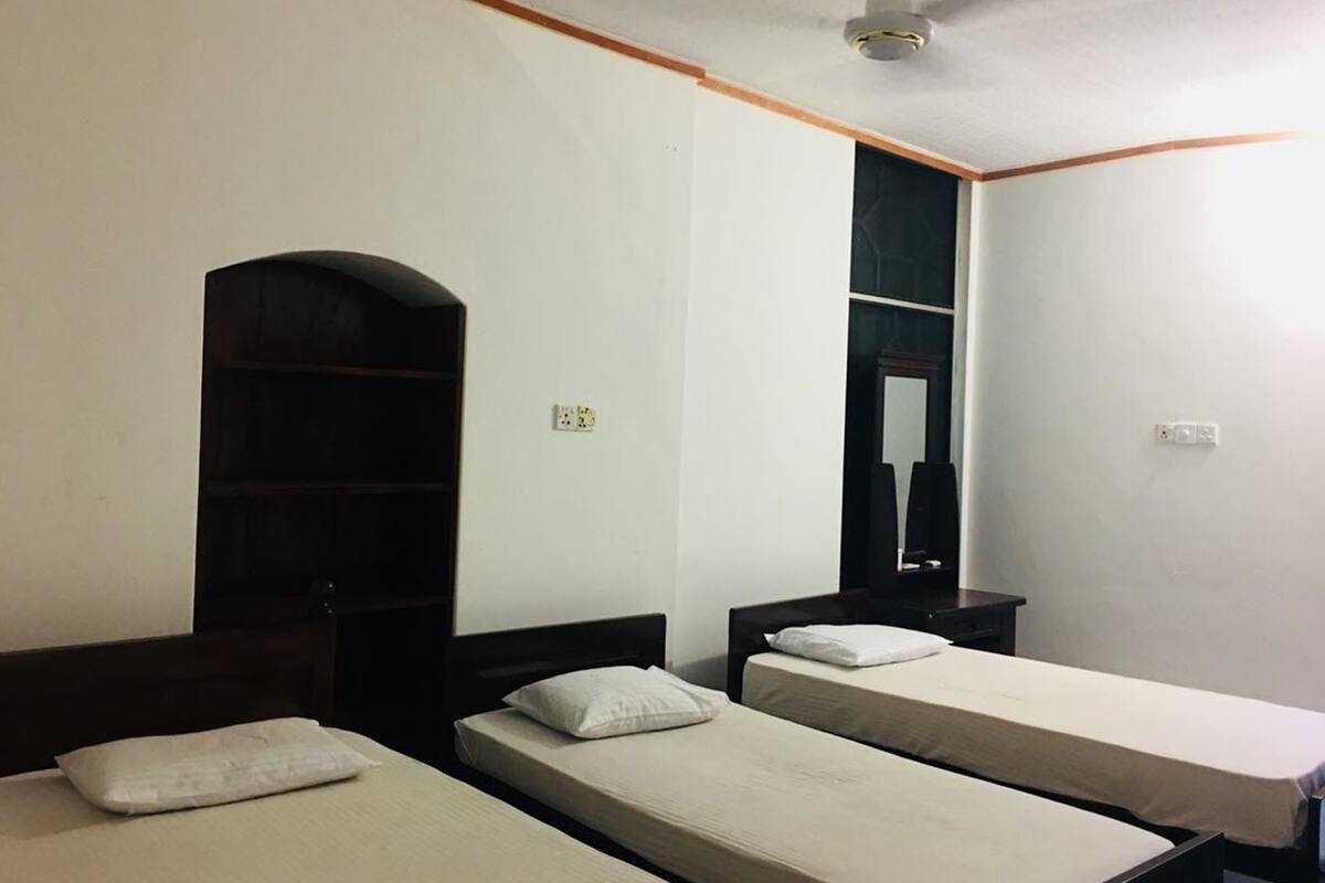 Quarto com duas camas de solteiro, guarda-roupa de madeira, espelho e ventoinha no teto.