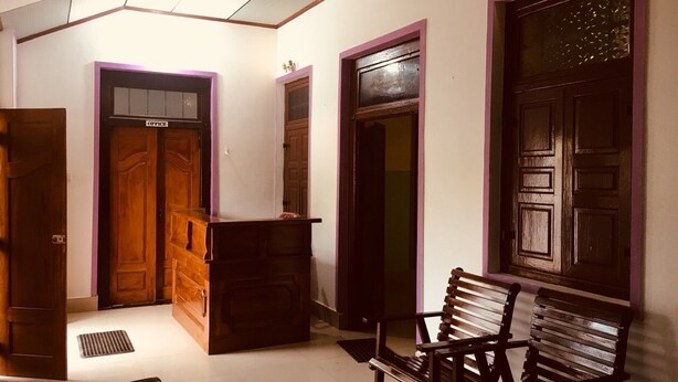 A hallway with wooden doors, a bench, and a ceiling fan. - Yarl Crown Inn (Kandy)