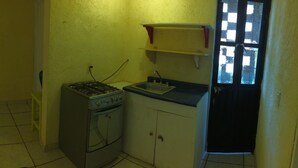 Een kleine keuken met een gasfornuis, een spoelbak en een eethoek met een tafel en stoelen. Er hangen drie ingelijste foto's aan de muur.
