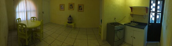 A compact kitchen with a gas stove, sink, and a dining area with a table and chairs. There are three framed pictures on the wall. - Departamentos Carolina (Dolores Hidalgo)