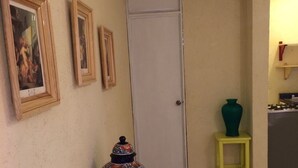 Een hal met betegelde vloer, een deur, een gele bank, een decoratieve vaas en lijstjes met afbeeldingen aan de muur.