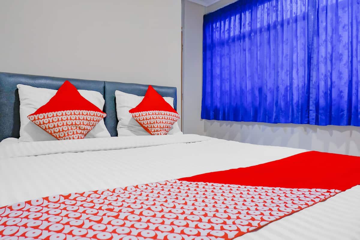 Ein Bett mit weißer Bettwäsche und Kissen in Rot-Weiß-Muster, eine rote Decke und ein blauer Vorhang.