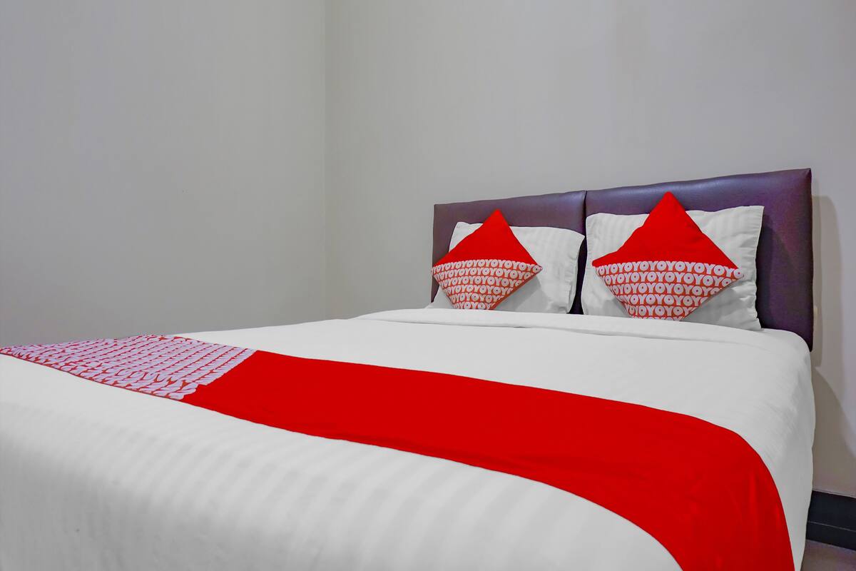 Ein Bett mit weißer und roter Bettdecke, zwei rote Kissen mit weißer Schrift und ein violettes Kopfteil.