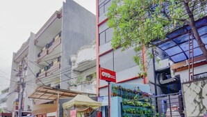 A multi-story building with balconies, a storefront with a sign, and a tree in front. - OYO 117 Blueberry Homestay (Jakarta)