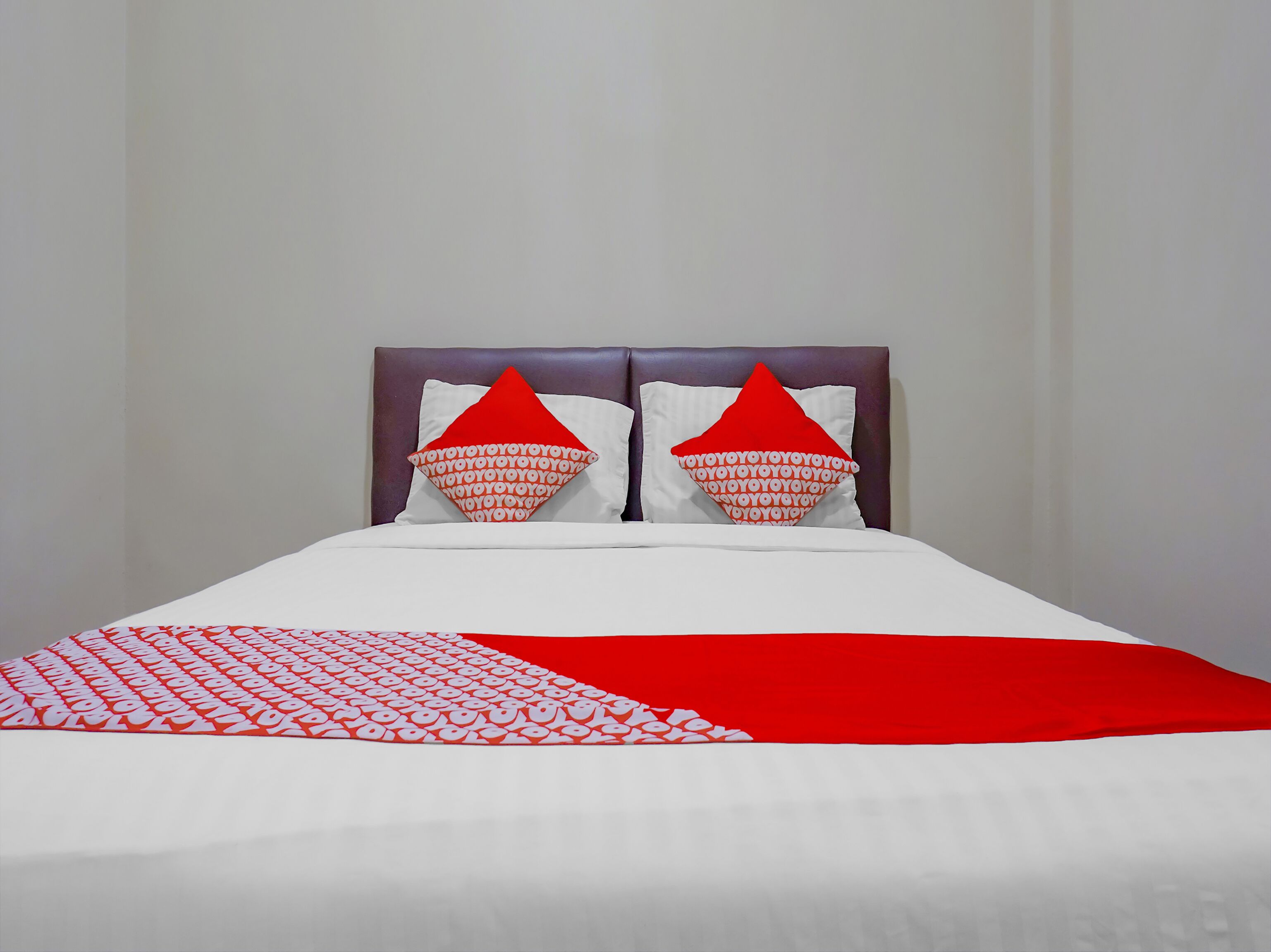 A bed with a white and red bedspread, two pillows with a red and white pattern, and a headboard.