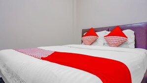 A neatly made bed with a white and red bedspread, two red pillows, and a purple headboard. - OYO 117 Blueberry Homestay (Jakarta)