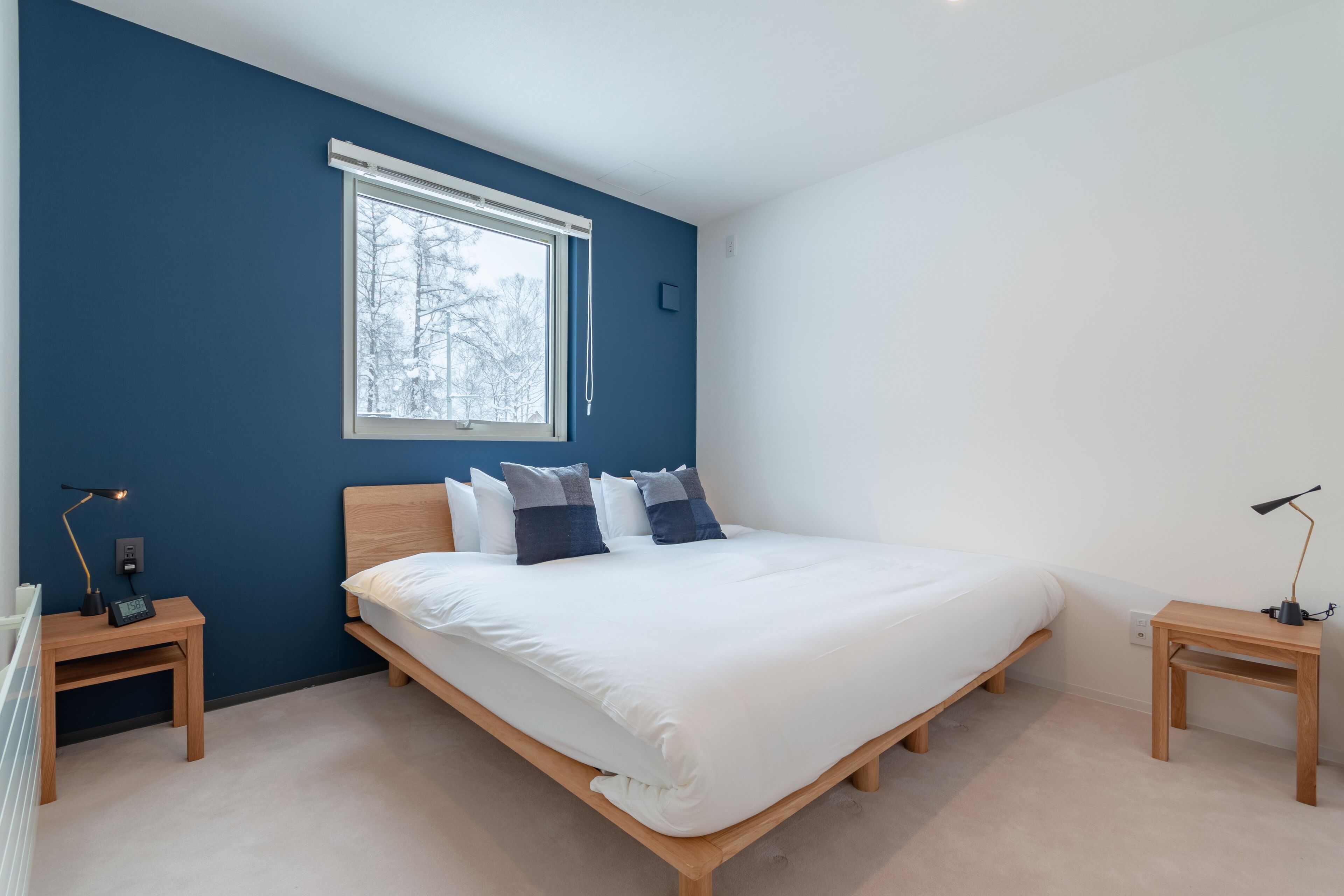 Quarto com uma cama grande, uma janela com vista para árvores e duas mesas de cabeceira com abajures.