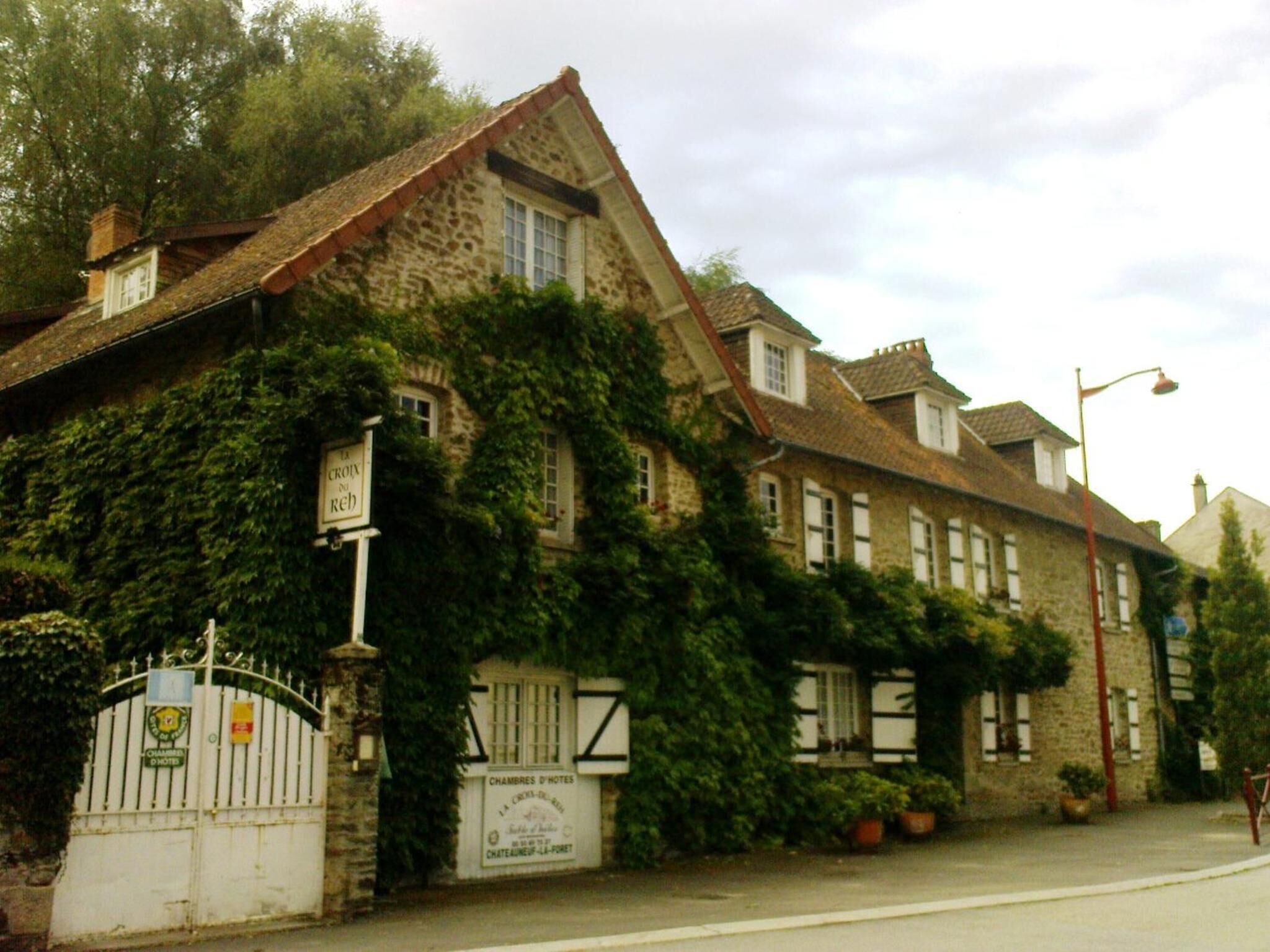 Un bâtiment en pierre dont les murs sont recouverts de lierre, avec une entrée fermée par un portail et des panneaux indiquant qu’il s’agit d’un hôtel.