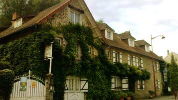 Un bâtiment en pierre dont les murs sont recouverts de lierre, avec une entrée fermée par un portail et des panneaux indiquant qu’il s’agit d’un hôtel.