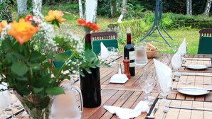 A wooden outdoor dining table set with wine glasses, plates, and a bottle of wine, surrounded by greenery. - La Croix du Reh (Châteauneuf-la-Forêt)