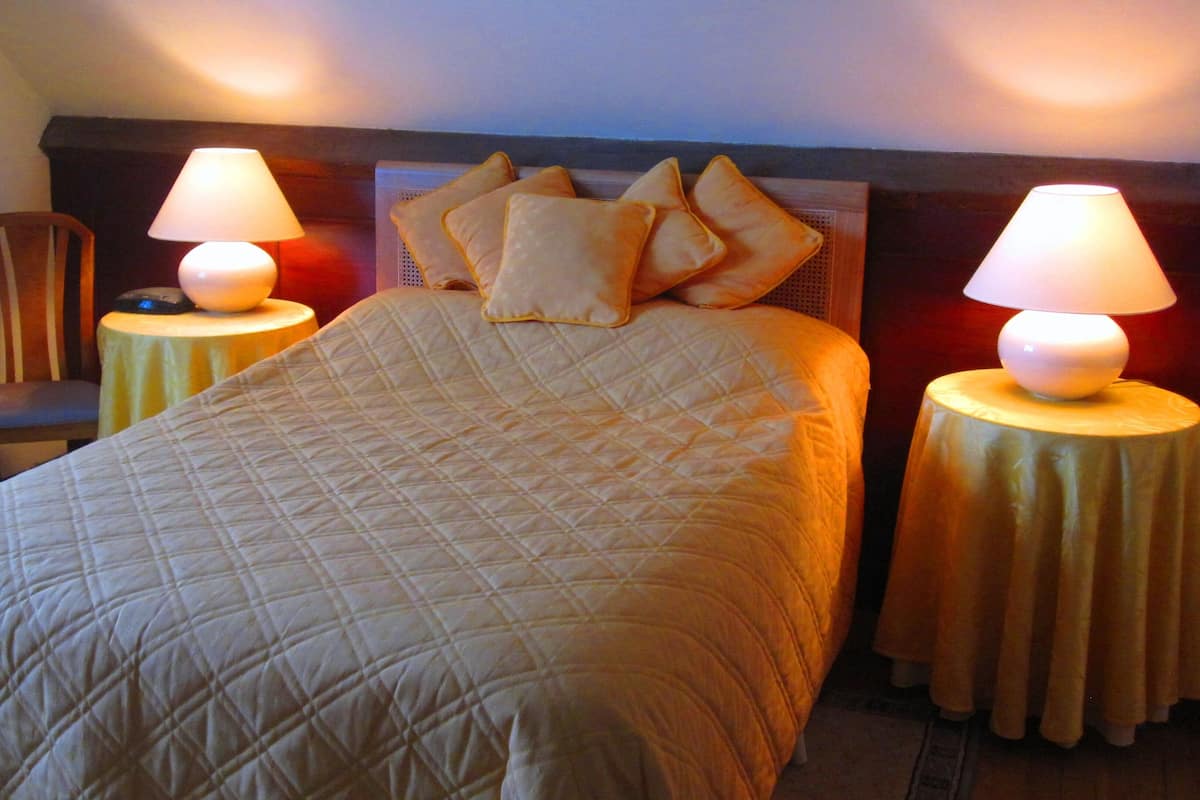 A neatly made bed with a quilted bedspread, flanked by two bedside tables with lamps, a chair, and a headboard.