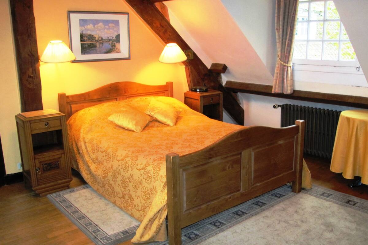 A bedroom with a wooden bed, two bedside tables, a nightstand, a framed picture on the wall, and a window with curtains.