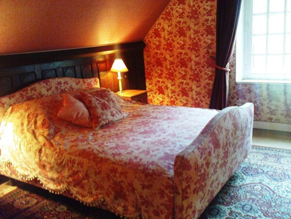 A bed with floral bedding, a nightstand with a lamp, and a window with curtains.