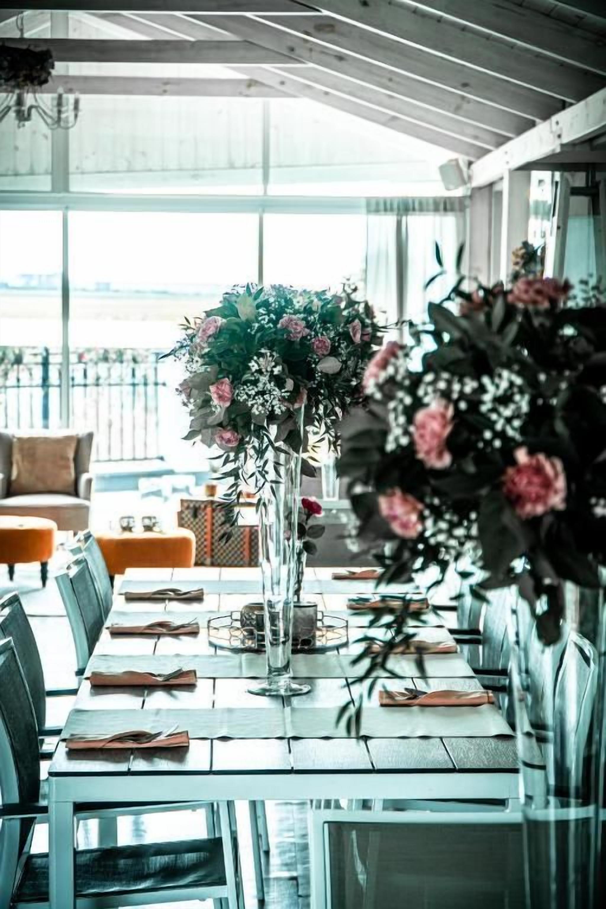 A dining area with a long table set for guests, featuring floral centerpieces and a view of the outdoors.