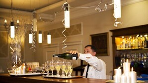 A bar setting with a bartender pouring a drink into glasses, a bar counter, and a display of bottles in the background.