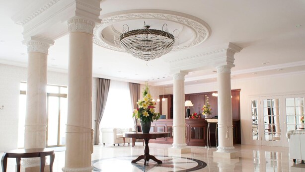 A spacious lobby with marble flooring, white columns, a central chandelier, and a reception desk.