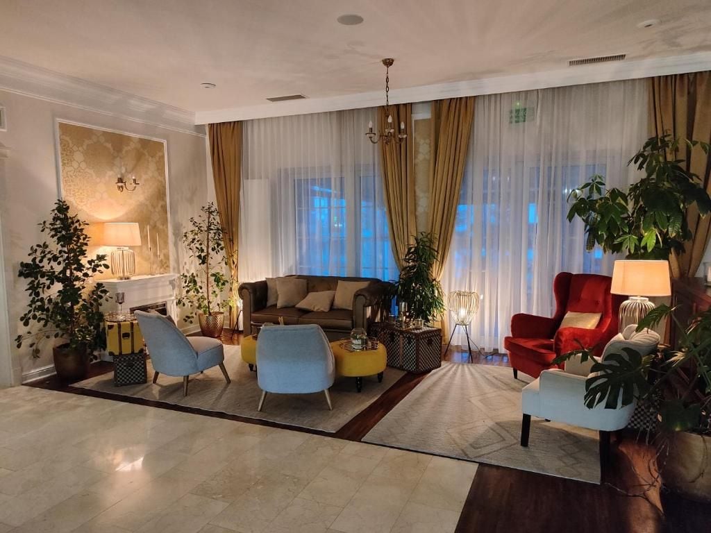 A spacious living room with a sofa, armchairs, and a red chair. There are potted plants and a lamp.