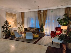Uma sala de estar ampla com sofá, poltronas e uma cadeira vermelha. Há plantas em vasos e um abajur.