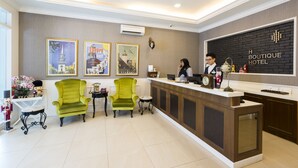 A hotel reception area with a reception desk, two green armchairs, a small table with a vase of flowers, and framed pictures on the wall. - H Boutique Hotel Sri Petaling (Kuala Lumpur)