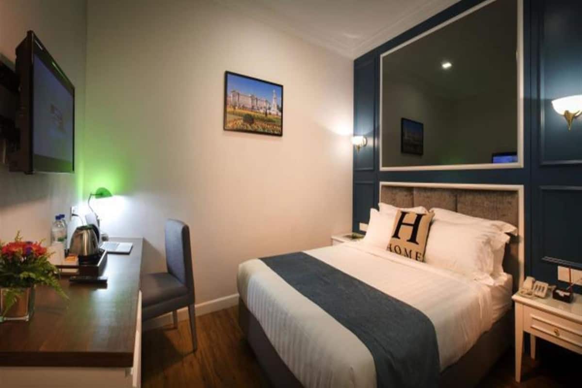 A hotel room with a bed, bedside table, desk, chair, and a large mirror.