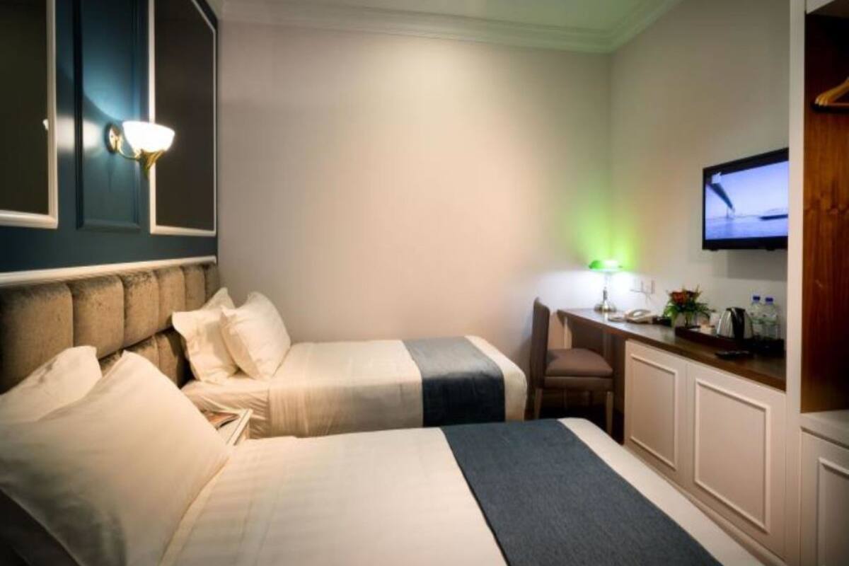 A hotel room with two beds, a desk, a chair, a television, and a wall-mounted light fixture.