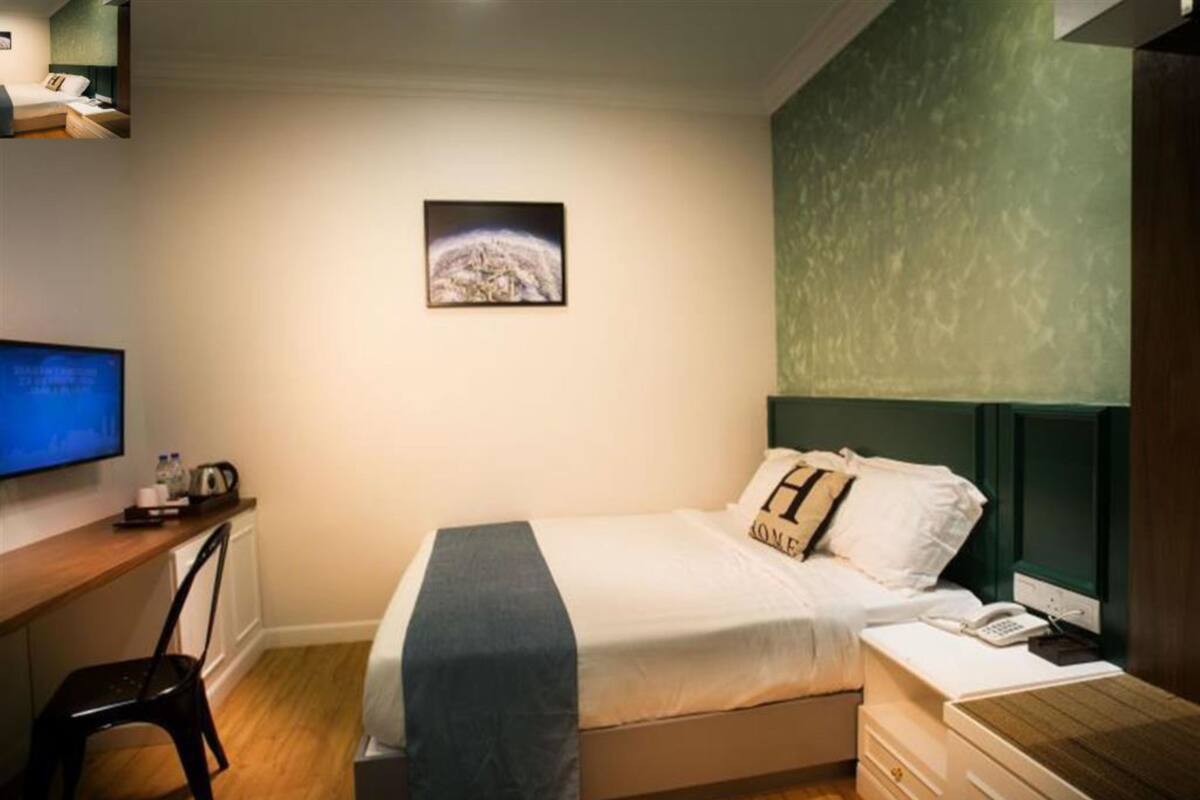 A bedroom with a bed, a desk with a computer, a chair, a telephone, and a picture on the wall.
