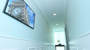 A hallway with white wainscoting, a framed picture of Big Ben, and a desk with a lamp. - H Boutique Hotel Sri Petaling (Kuala Lumpur)