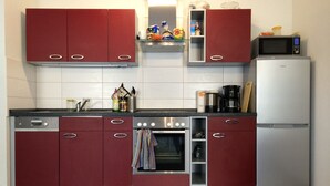 A kitchen with red cabinets, a dishwasher, an oven, a microwave, and a refrigerator. - Bett & Bike Eden (Senftenberg)