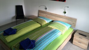 A double bed with green and blue striped bedding, a wooden headboard, and a nightstand with a remote control. - Bett & Bike Eden (Senftenberg)