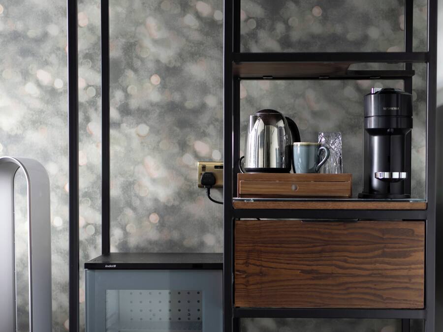 Una kitchenette compacta con refrigerador integrado, cafetera y hervidor en un estante.