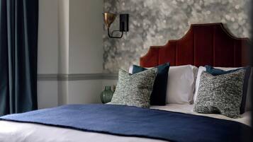 A neatly made bed with a dark blue bedspread, white pillows, and green and blue patterned pillows. A red headboard and a wall-mounted lamp are visible.