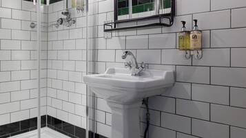 Un baño con un lavamanos pedestal blanco, cabina de ducha con mampara de vidrio y suelo de baldosas con diseño geométrico.