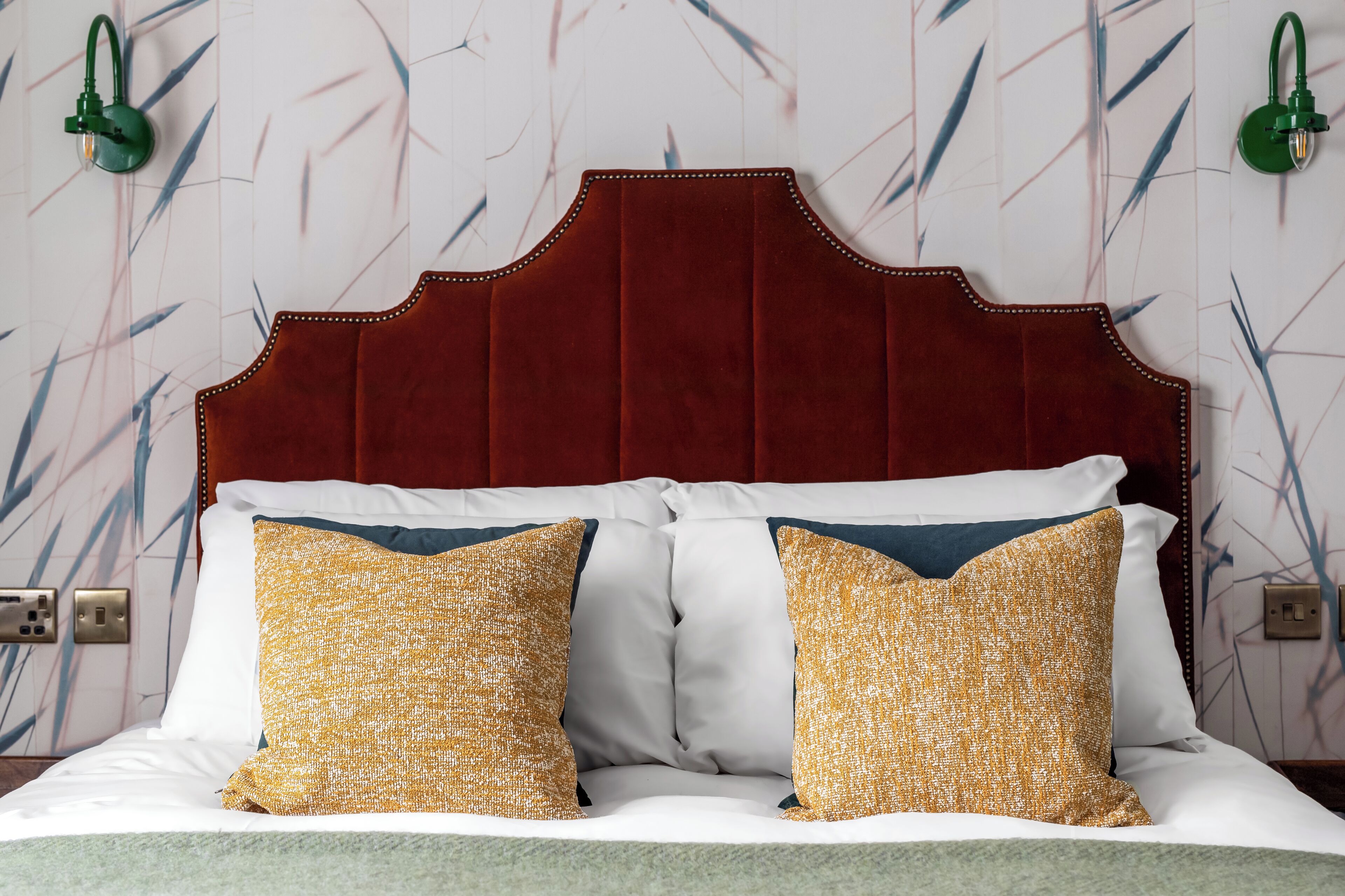A bed with a red headboard, white bedding, and two patterned pillows.