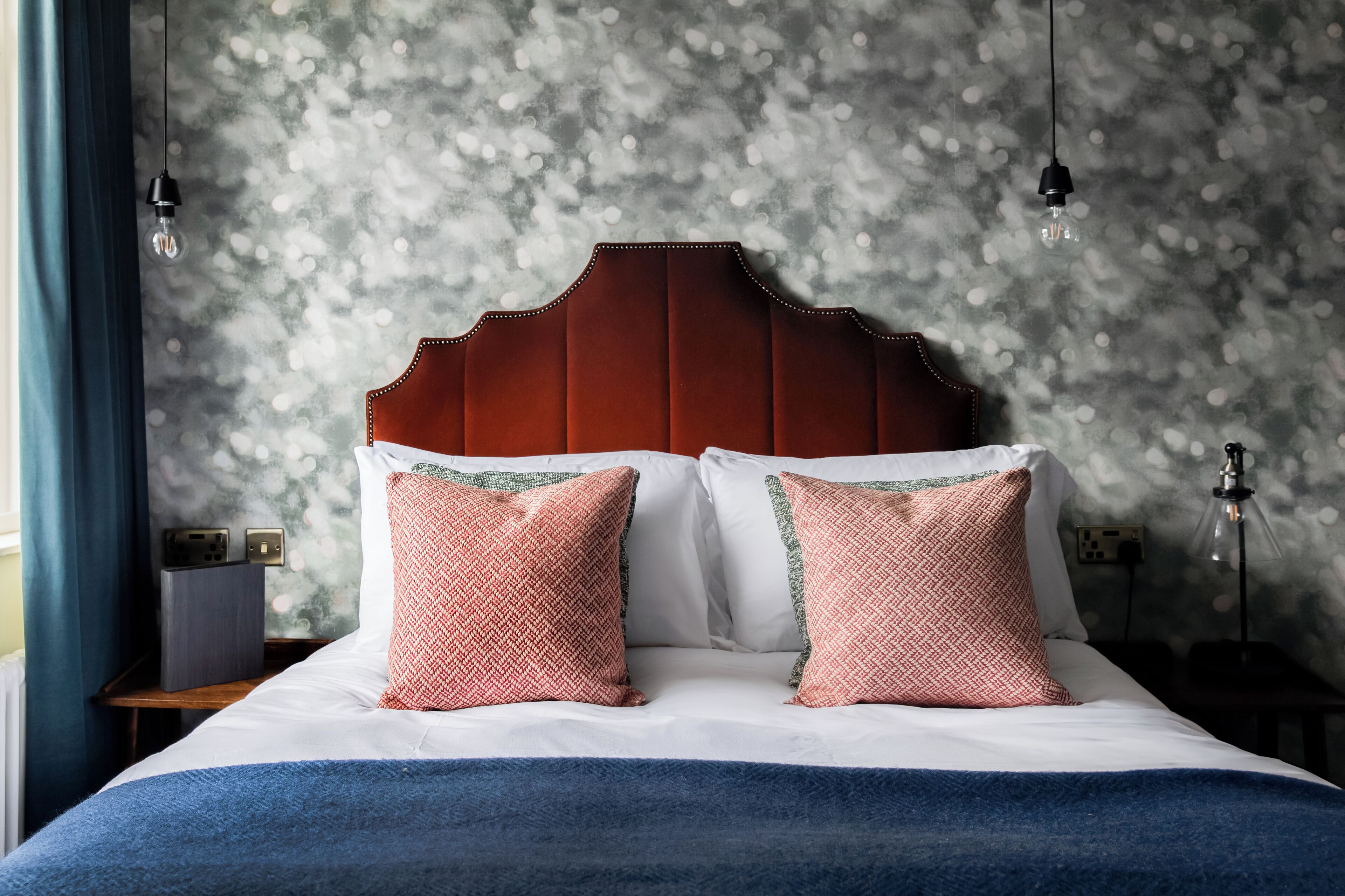 A neatly made bed with a wooden headboard, two patterned pillows, and a blue blanket.
