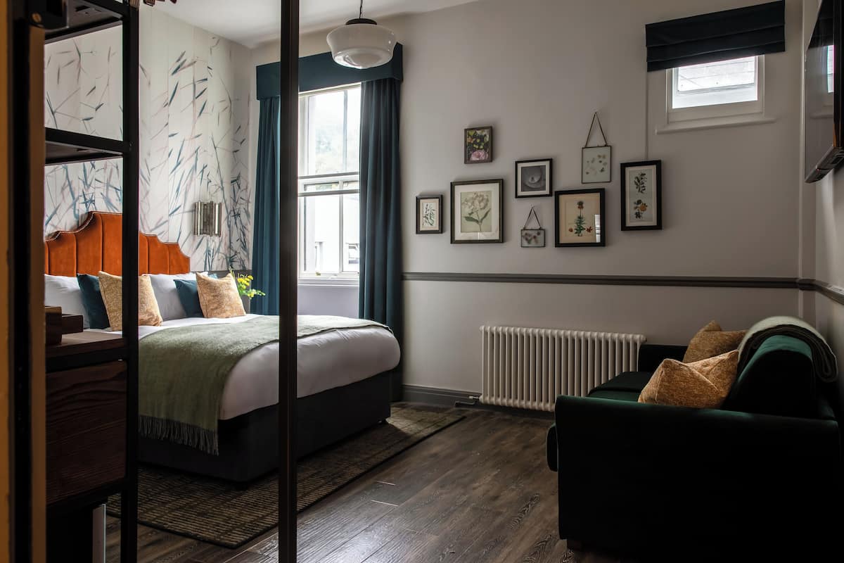 A modern bedroom with a bed, a green armchair, a radiator, and framed artwork on the wall.