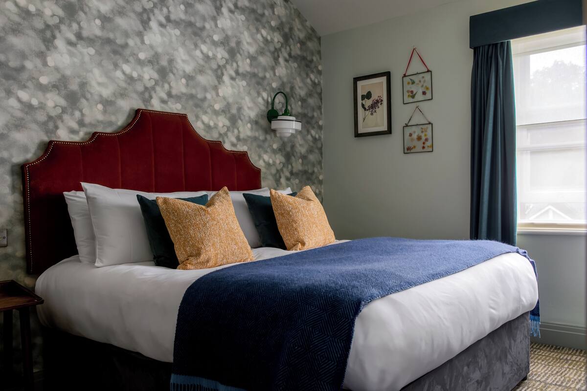 A neatly made bed with a red headboard, white and blue bedding, and decorative pillows.