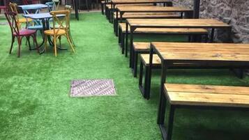 Ein Restaurant mit Holztischen und -stühlen, grüner Kunstrasen und einer Steinwand.