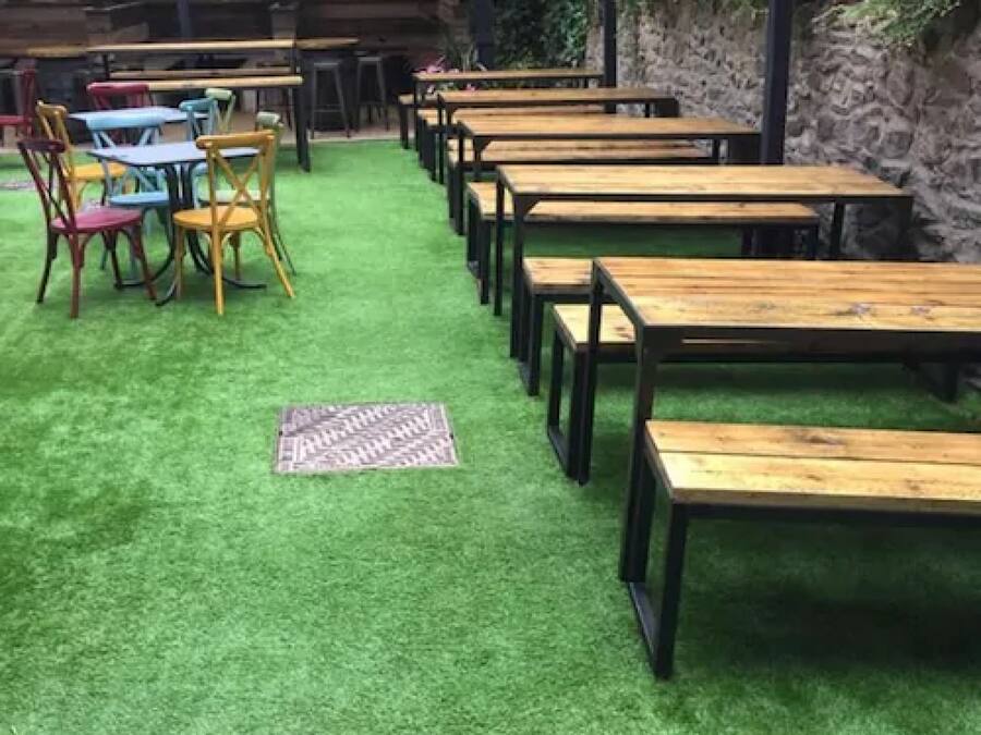 Ein Restaurant mit Holztischen und -stühlen, grüner Kunstrasen und einer Steinwand.