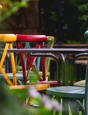 A row of outdoor metal chairs with colorful handles, arranged on a patio with a wooden fence and greenery in the background.