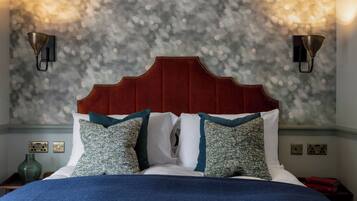 A bed with a red headboard, white and teal pillows, and a blue blanket. There are two wall sconces on either side of the bed.
