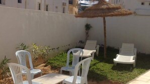 Een terras met witte plastic stoelen en een tafel, omgeven door een lage muur en een palmboom.